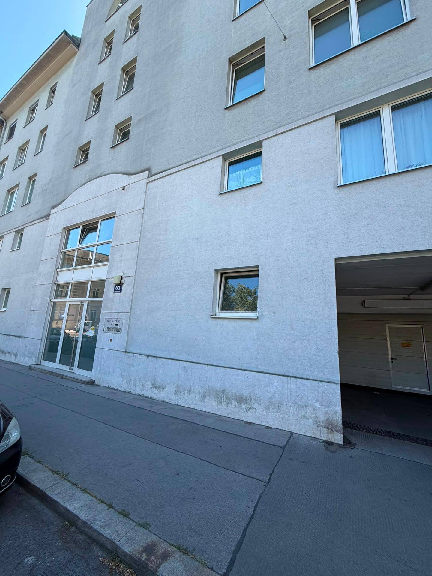Fassade eines Mehrfamilienhauses mit Haupteingang und offener Einfahrt zu einer Tiefgarage.
