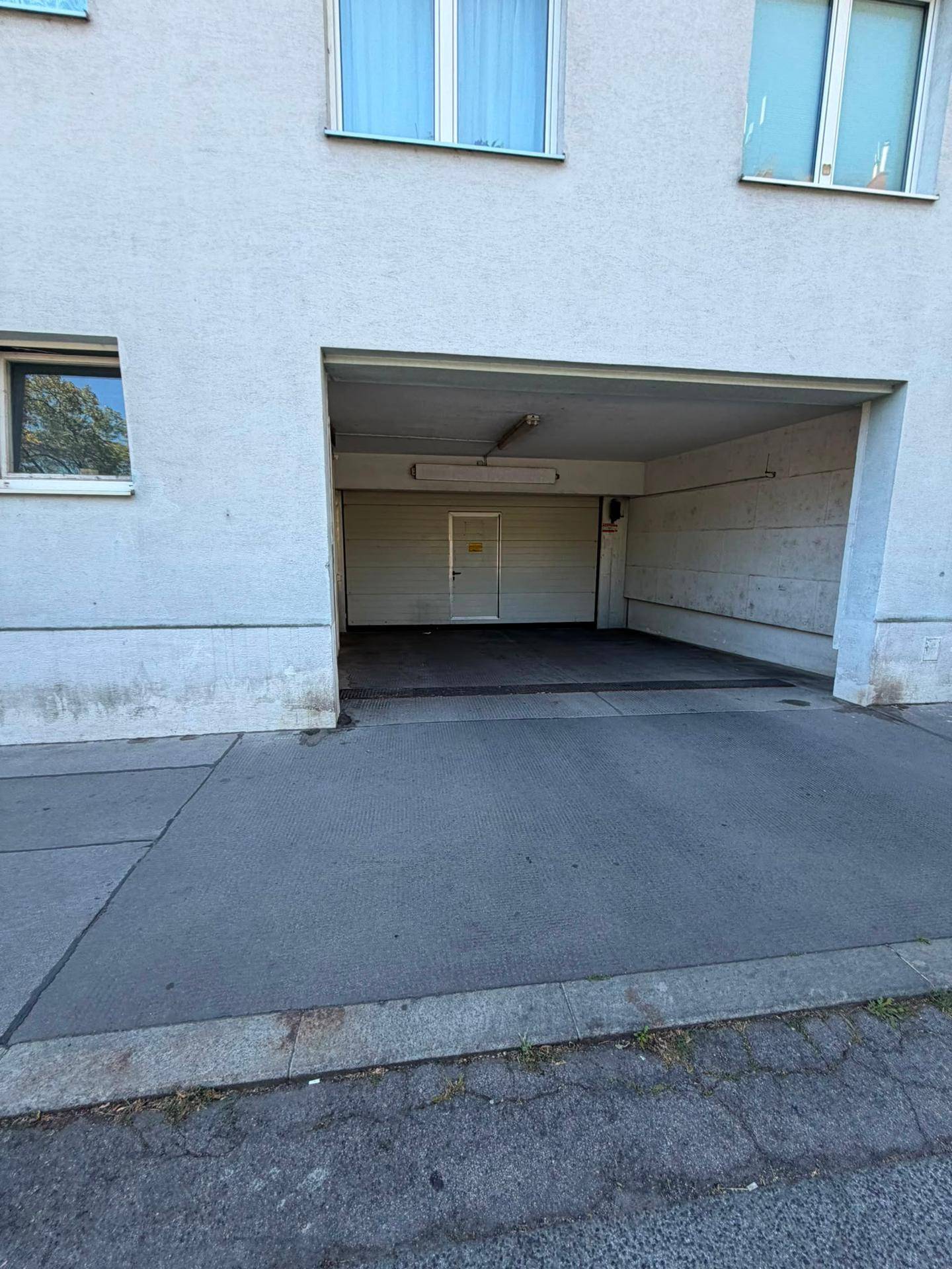 Gebäudefassade mit offener Einfahrt zu einer Tiefgarage, die einen Blick ins Innere gewährt.