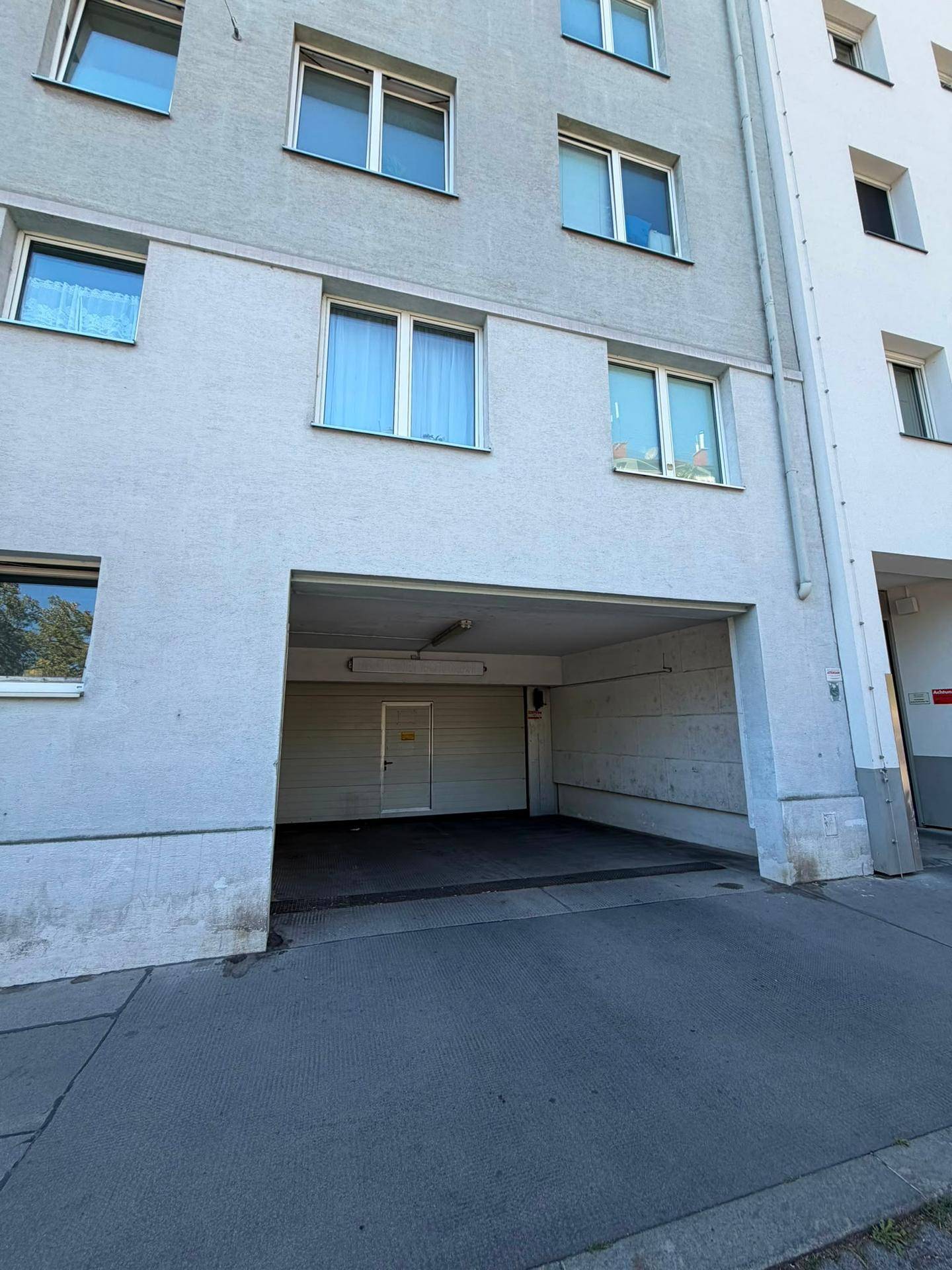 Gebäudefassade mit offener Einfahrt zu einer Tiefgarage, die einen Blick ins Innere gewährt.