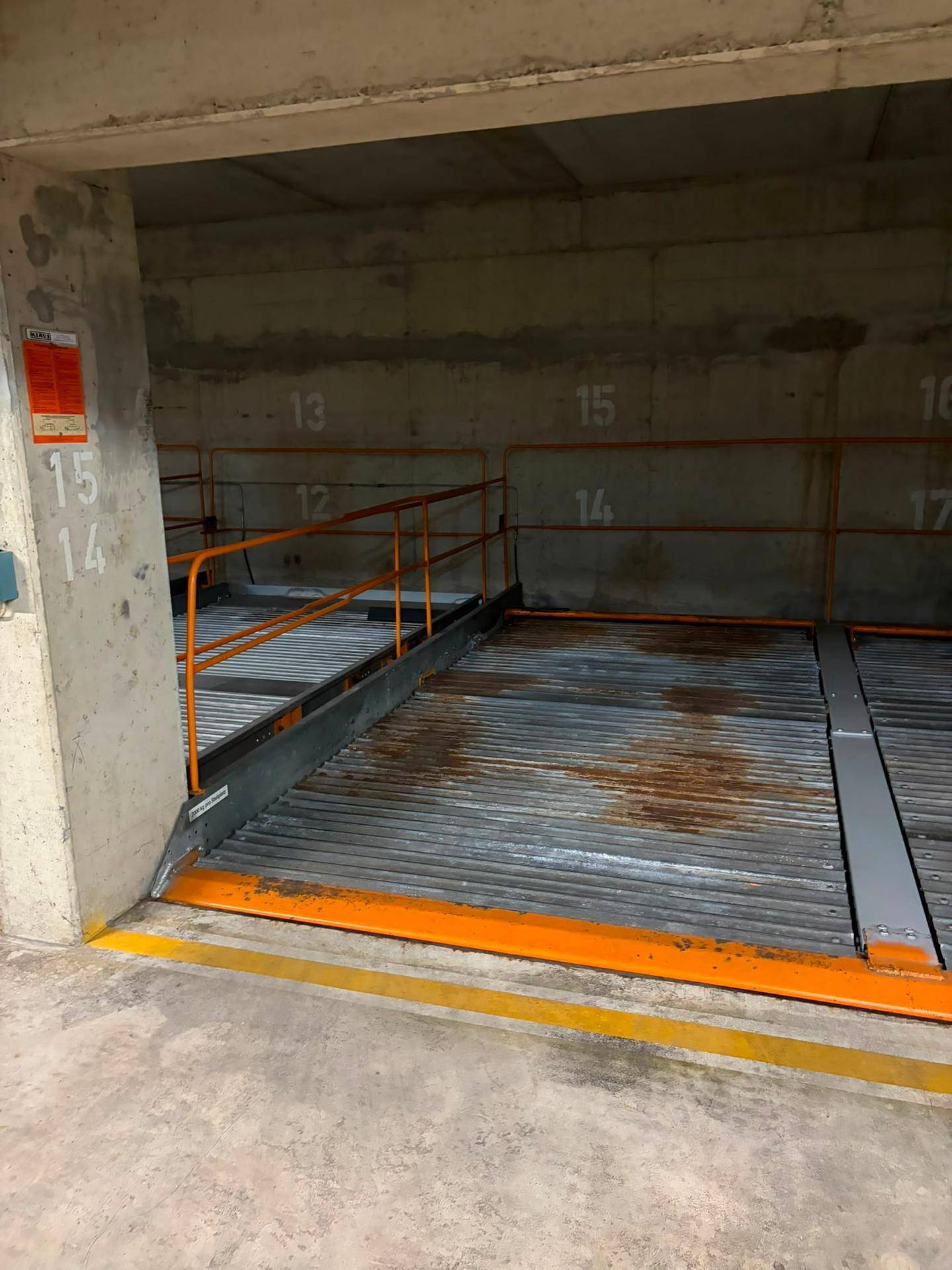 Mechanisches Doppelparkersystem in einer Tiefgarage mit nummerierten Stellplätzen und orangefarbenen Sicherheitsgeländern.