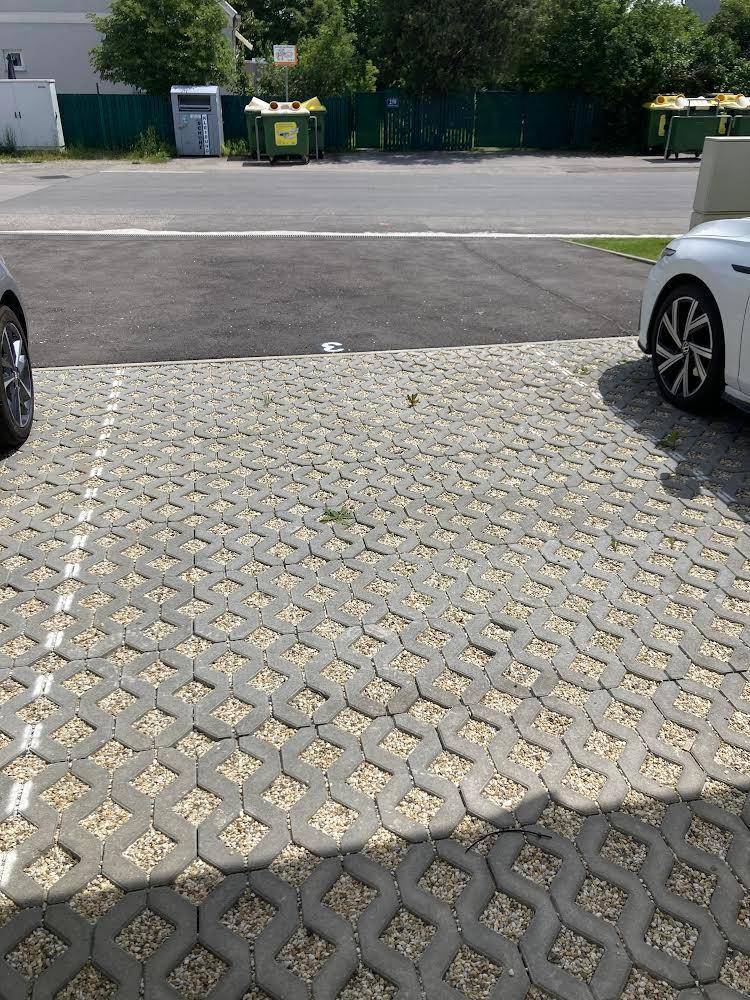 Außenbereich mit Parkplätzen, Müllcontainern und Bäumen im Hintergrund, gut gepflegt.