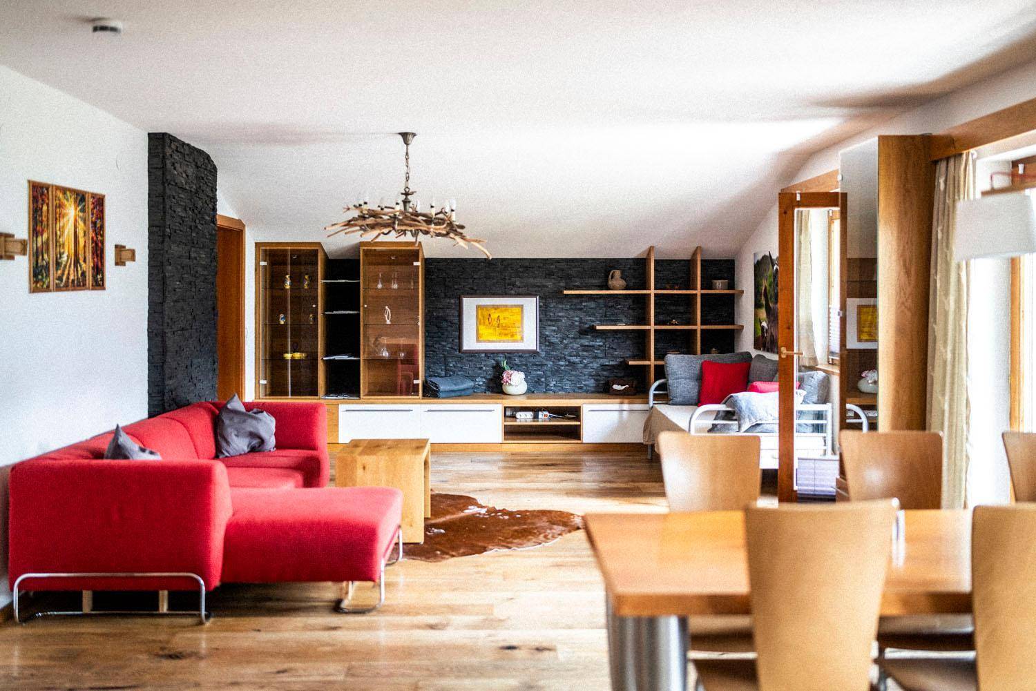 Geräumiger Wohn-Essbereich mit rotem Sofa, Holzboden und dunkler Steinwand, offen gestaltet.