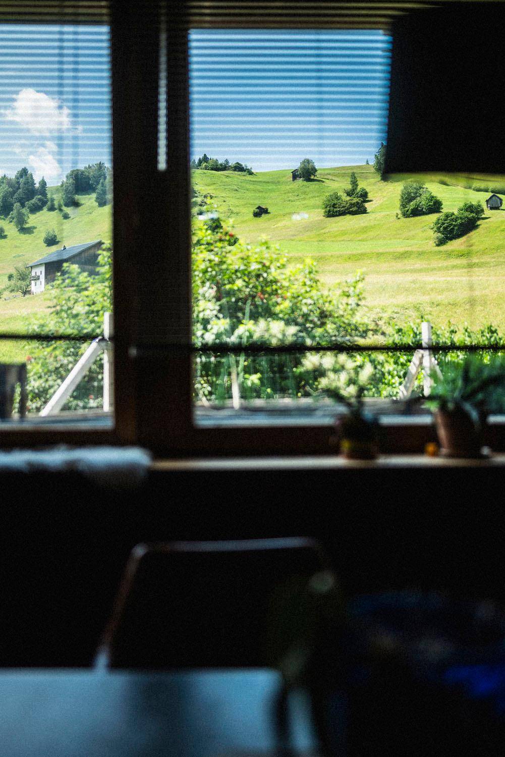 Fensterblick auf eine idyllische grüne Hügellandschaft mit vereinzelten Häusern.
