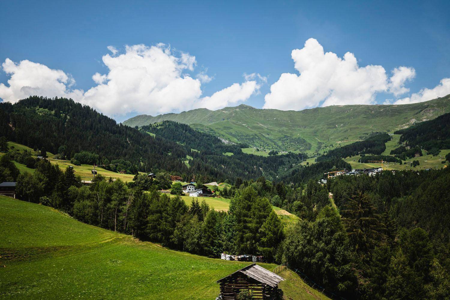Weitläufige grüne Berglandschaft mit bewaldeten Hängen und einem kleinen Dorf in der Ferne.