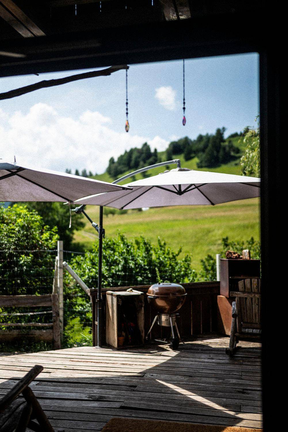 Holzterrasse mit Grillbereich und weitem Blick über grüne Hügel und Wälder.