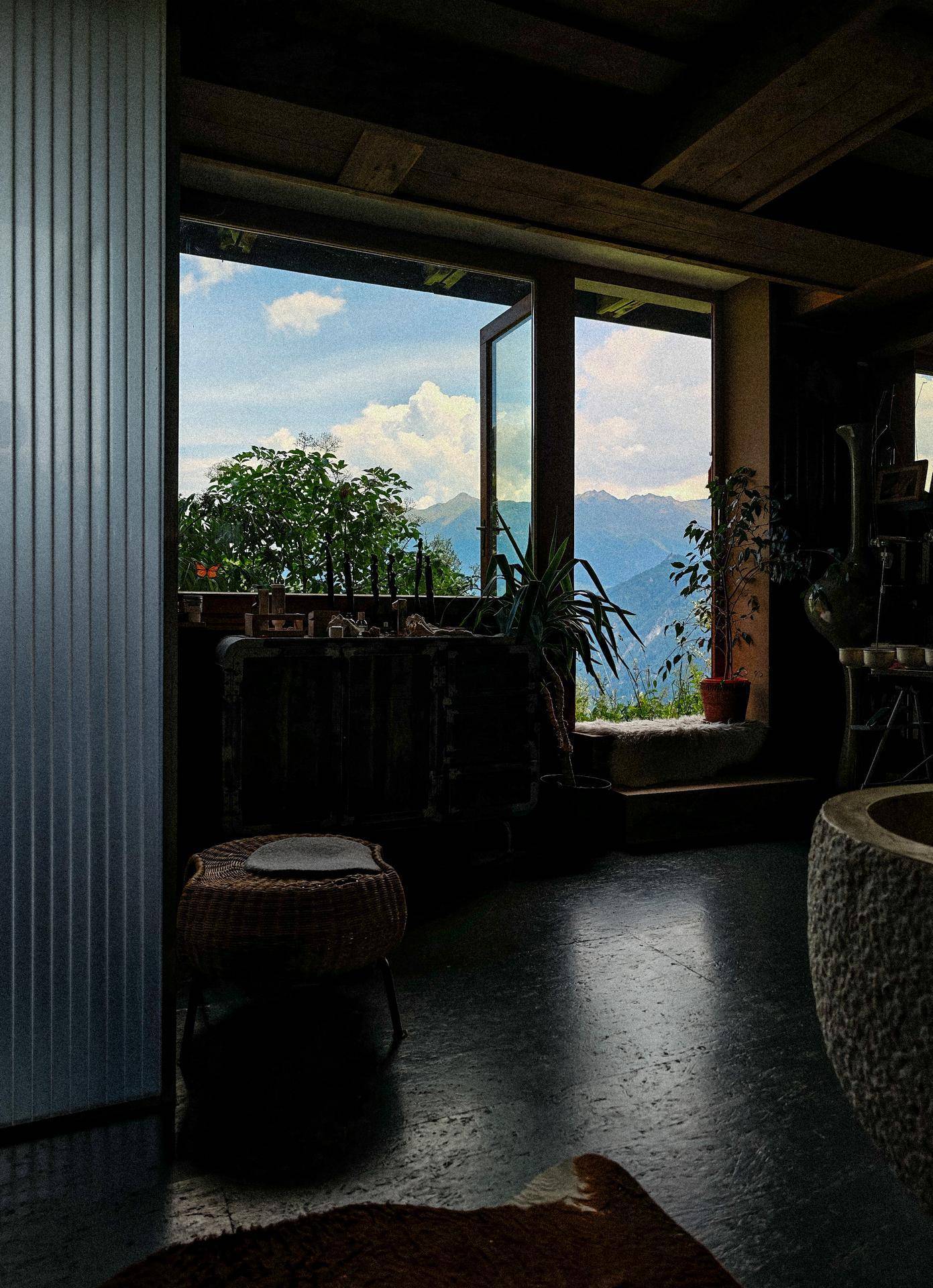 Innenraum mit Bergblick durch offene Fenster, dunklem Boden und rustikalen Möbeln.