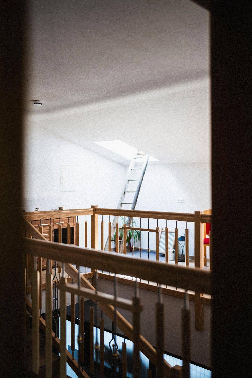 Heller Flur mit Holzgeländer und einer Leiter, die zu einem Dachfenster im Dachgeschoss führt.