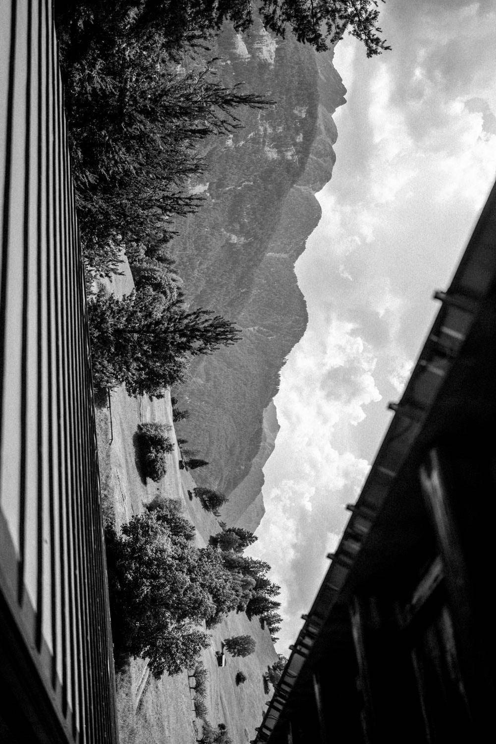 Schwarz-Weiß-Aufnahme einer majestätischen Berglandschaft unter bewölktem Himmel, umrahmt von Gebäudeteilen.