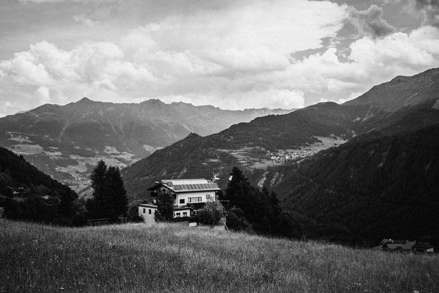 Schwarz-Weiß-Aufnahme eines Hauses mit Solarpaneelen auf dem Dach, eingebettet in eine weite Berglandschaft.