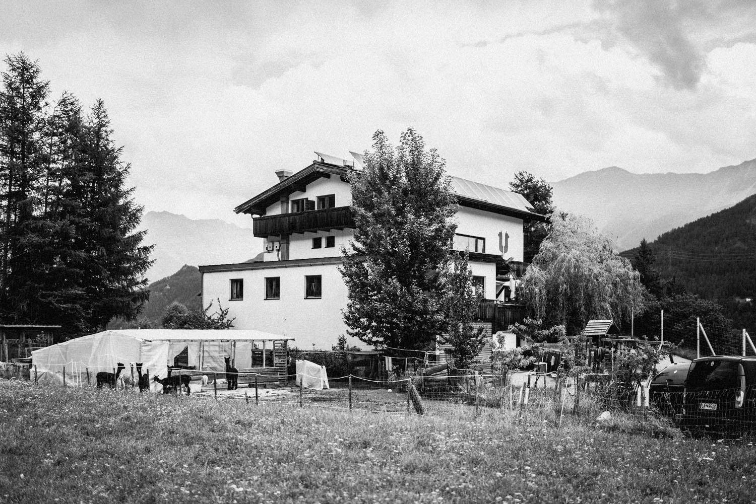 Schwarz-Weiß-Bild eines Hauses im alpinen Stil mit Solarpaneelen und einem Gehege im Vordergrund.