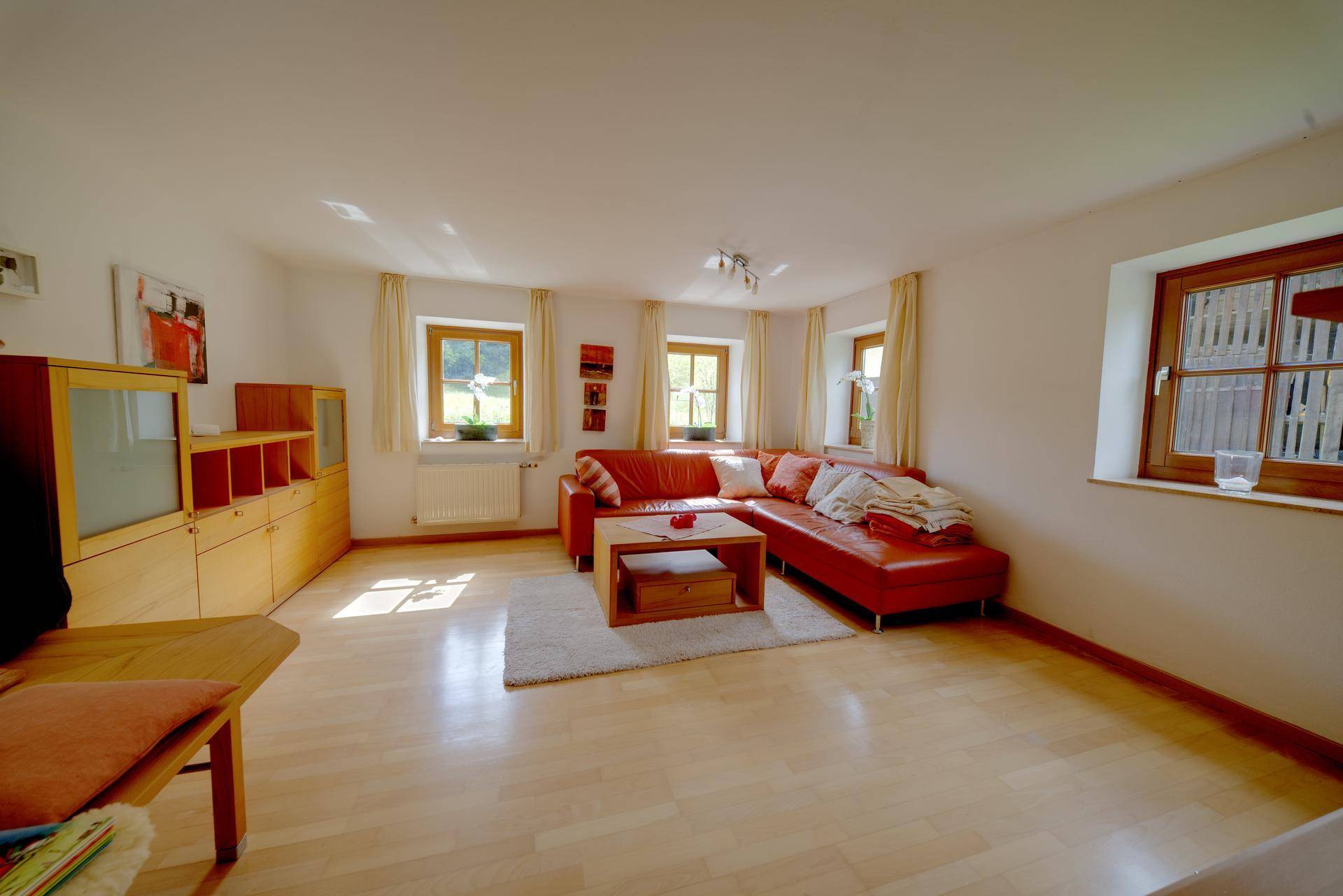 Gemütliches Wohnzimmer mit rotem Sofa, hellem Holzboden und mehreren Fenstern.
