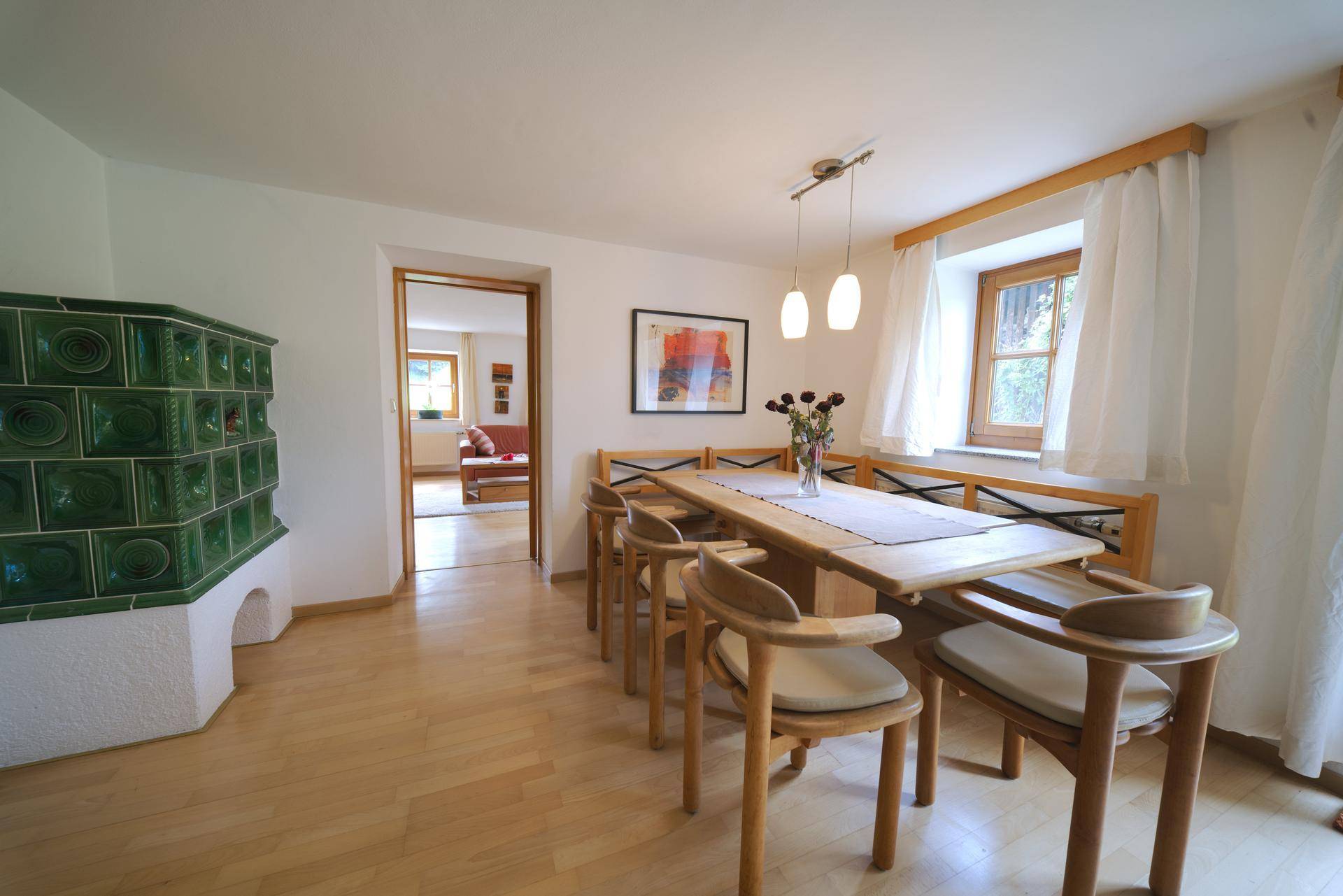 Traditioneller Essbereich mit großem Holztisch, Kachelofen und Zugang zum Wohnzimmer.