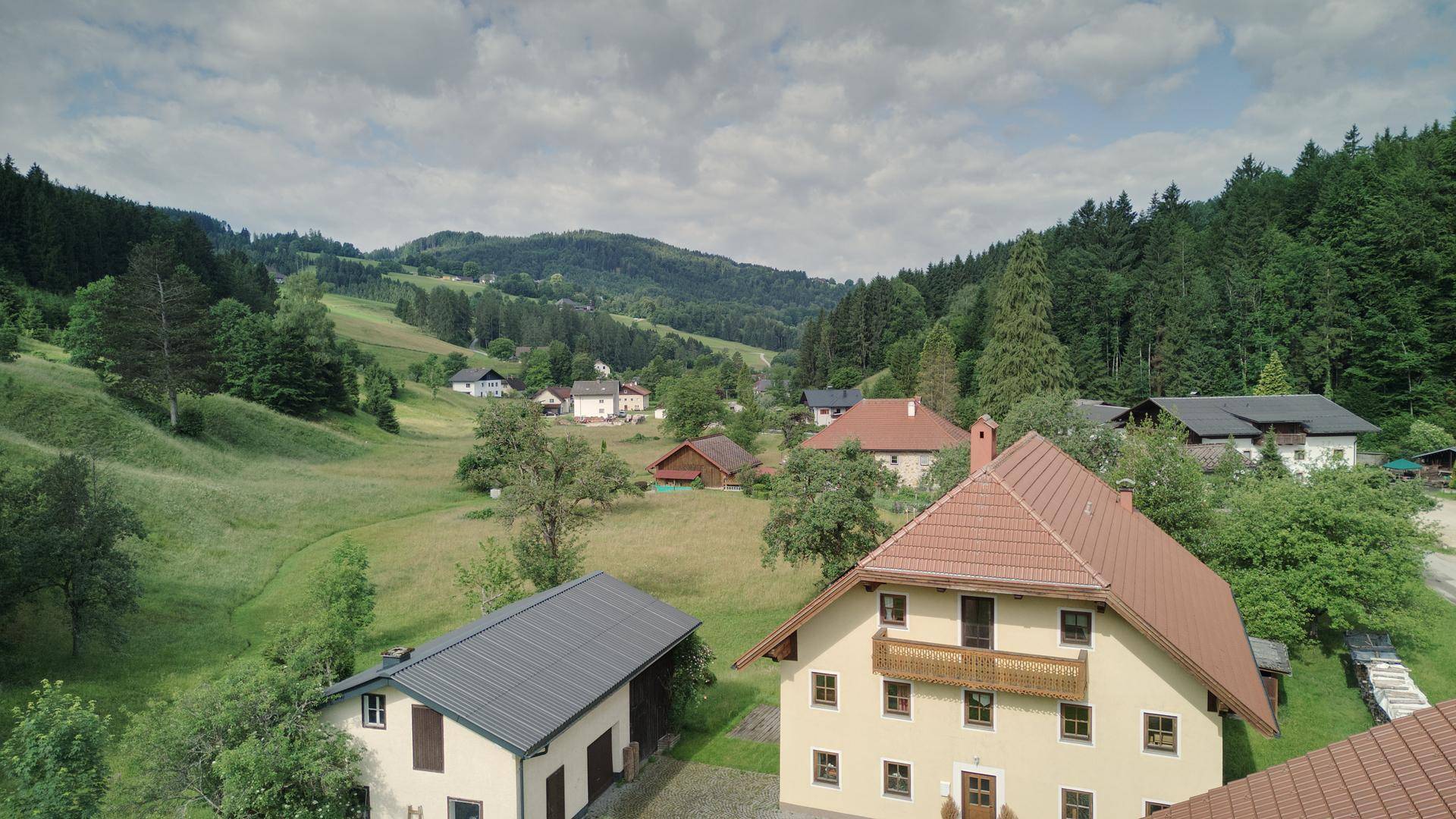 Malerische Landschaft mit mehreren Häusern und viel Grün, unter einem bewölkten Himmel.