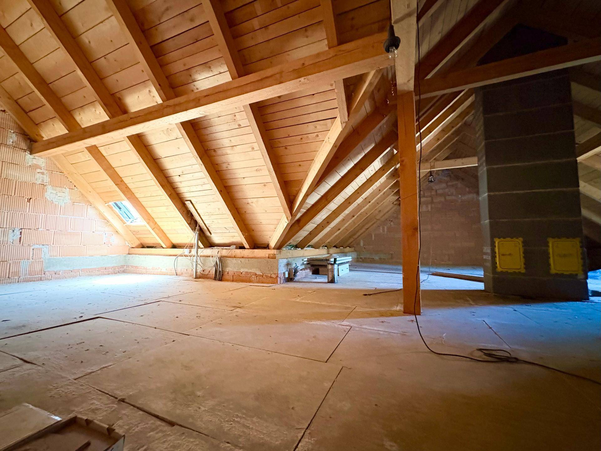Unausgebauter Dachboden mit sichtbaren Holzbalken und Ziegelwänden, bereit für den Ausbau.