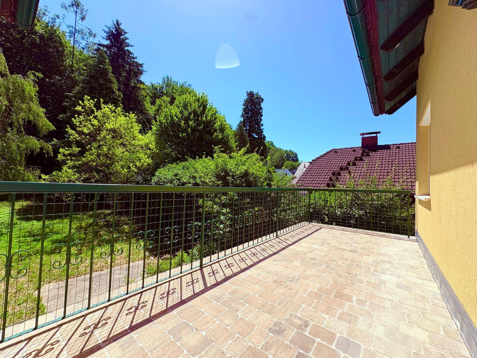 Geräumiger Balkon mit Fliesenboden und Metallgeländer, umgeben von üppigem Grün.
