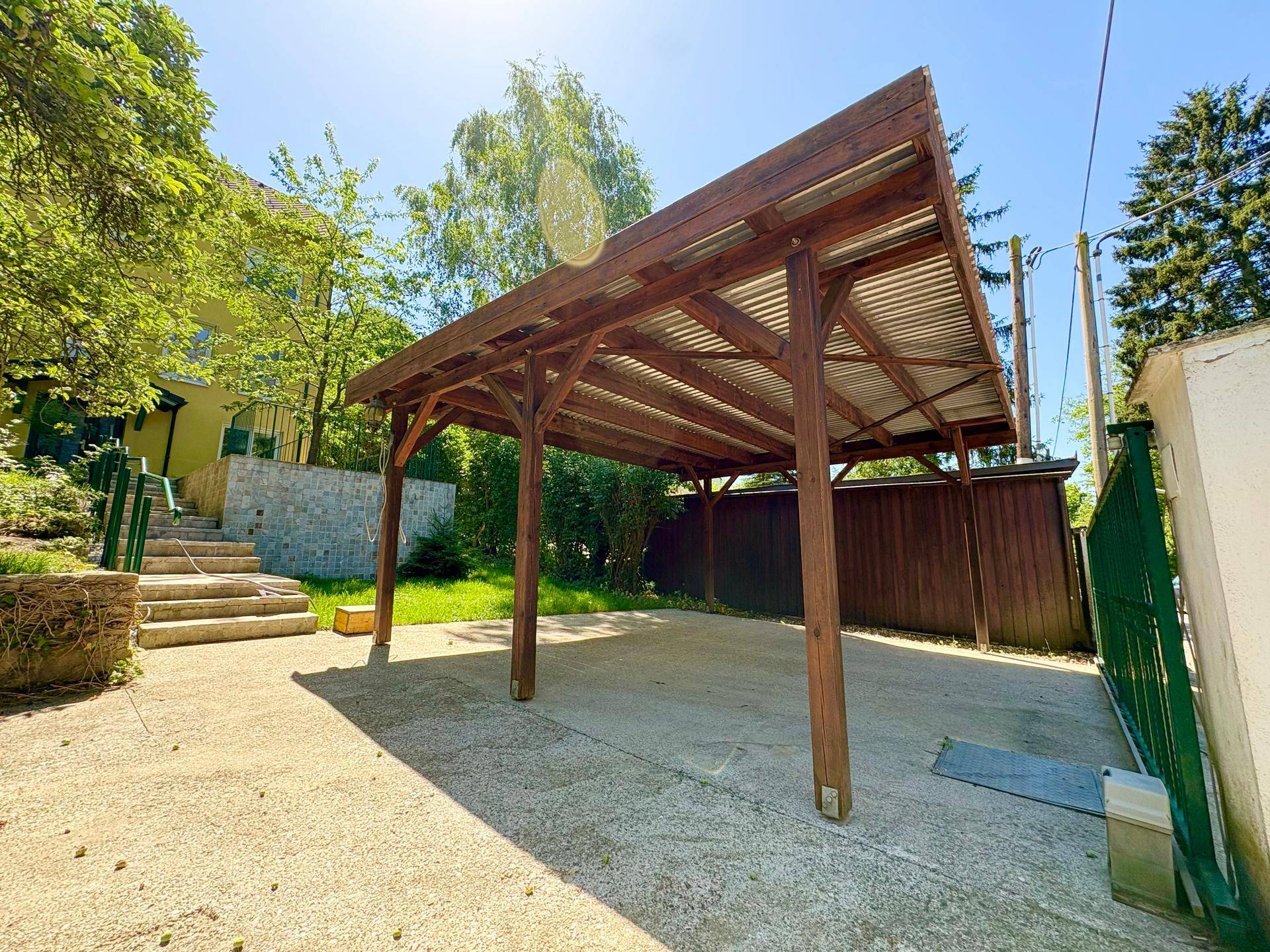 Überdachter Stellplatz aus Holz für Fahrzeuge, umgeben von Grün und sonnigem Wetter.