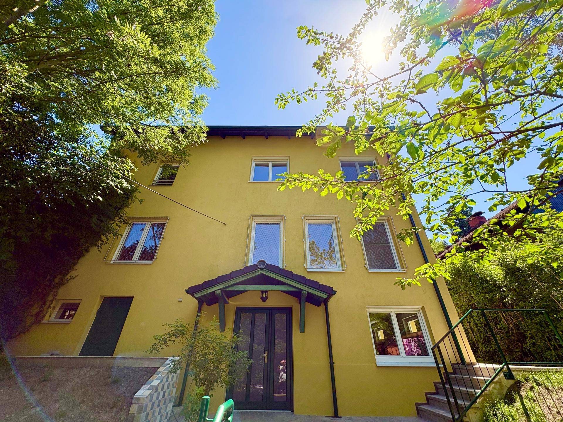 Die sonnige Fassade des Hauses mit mehreren Fenstern und einem überdachten Eingangsbereich.