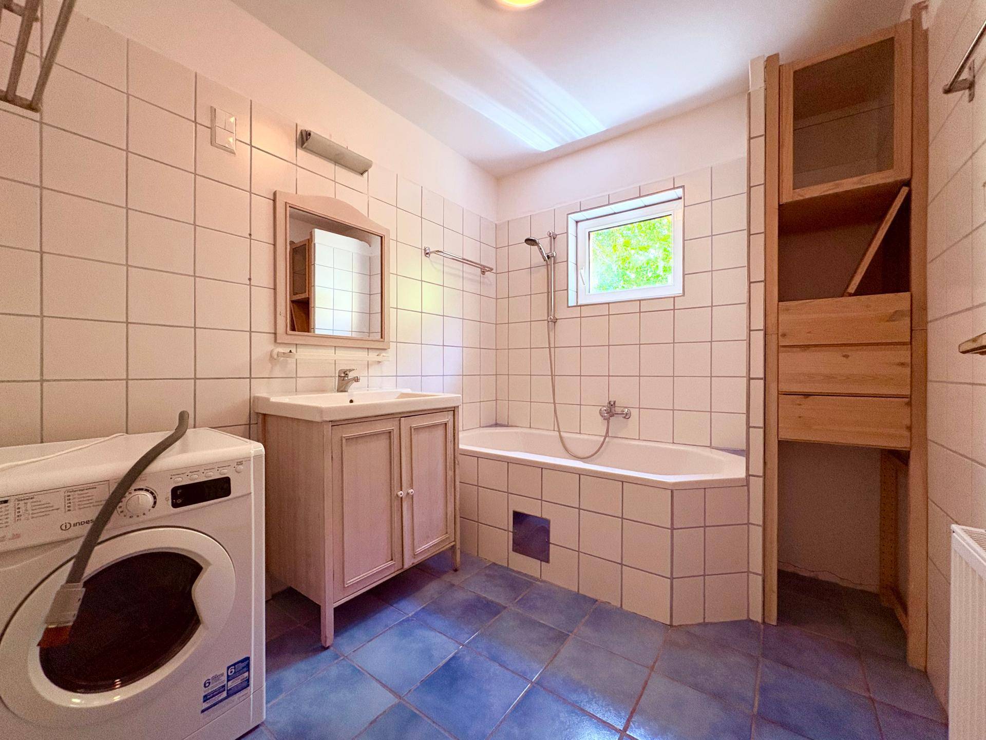 Badezimmer mit blauen Fliesen, Badewanne, Waschmaschine und einem Fenster für Tageslicht.