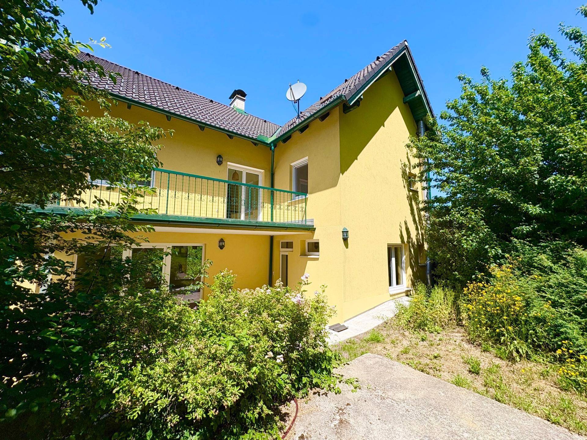 Rückansicht des gelben Hauses mit Balkon und umgebender grüner Natur.