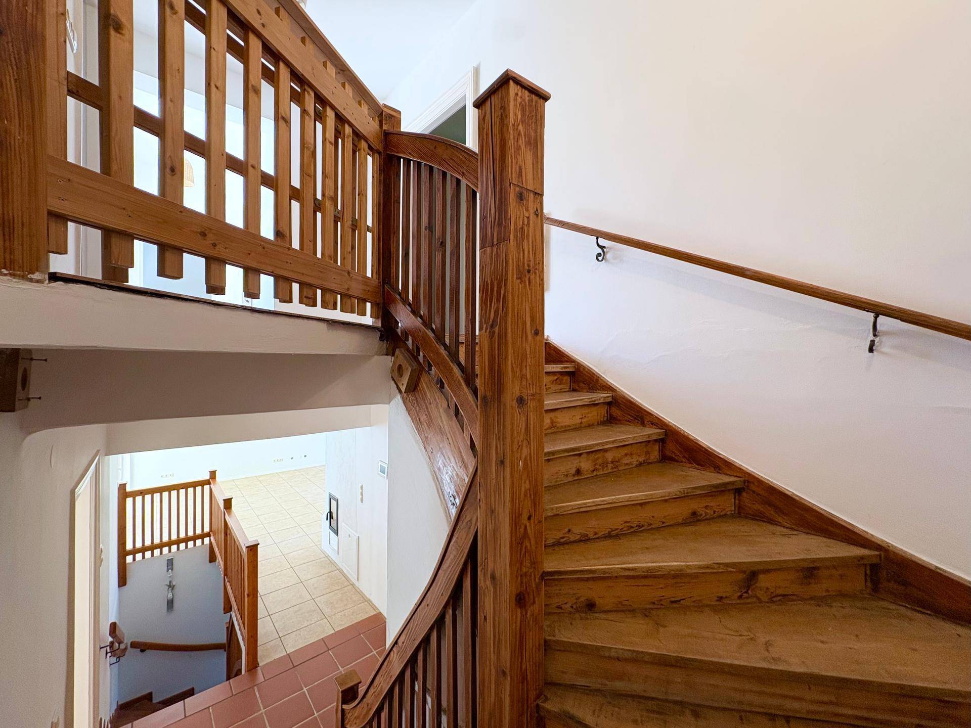 Geschwungene Holztreppe mit Geländer, die die verschiedenen Etagen des Hauses verbindet.