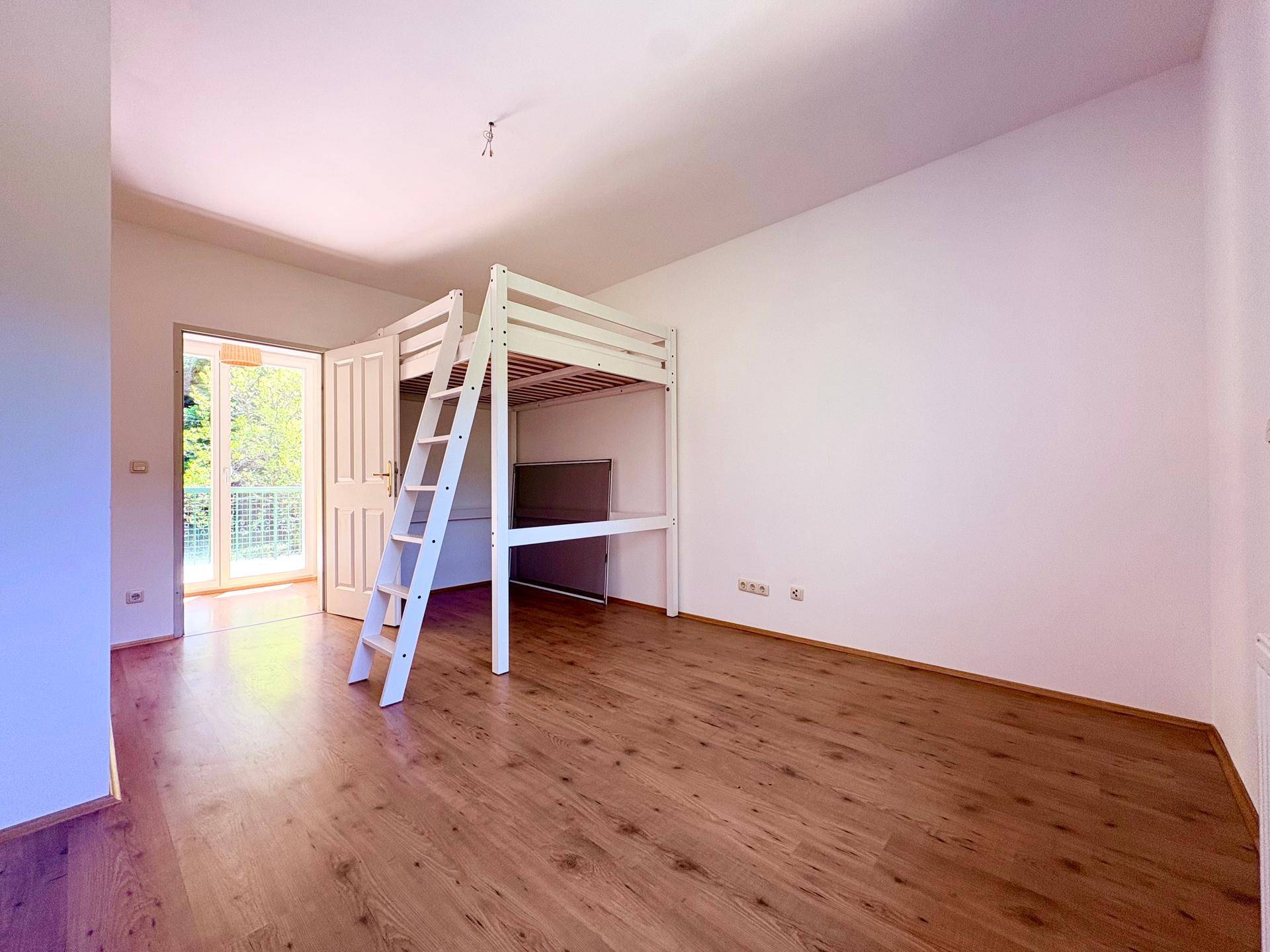 Kinderzimmer mit Hochbett, Holzboden und Zugang zu einem Balkon mit Blick ins Grüne.