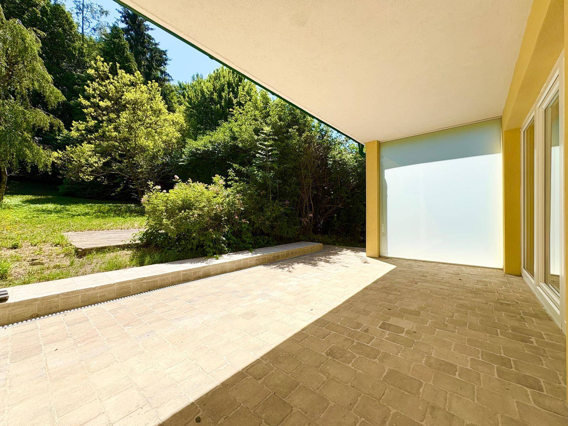 Überdachte Terrasse mit Fliesenboden und Blick auf den grünen Gartenbereich.