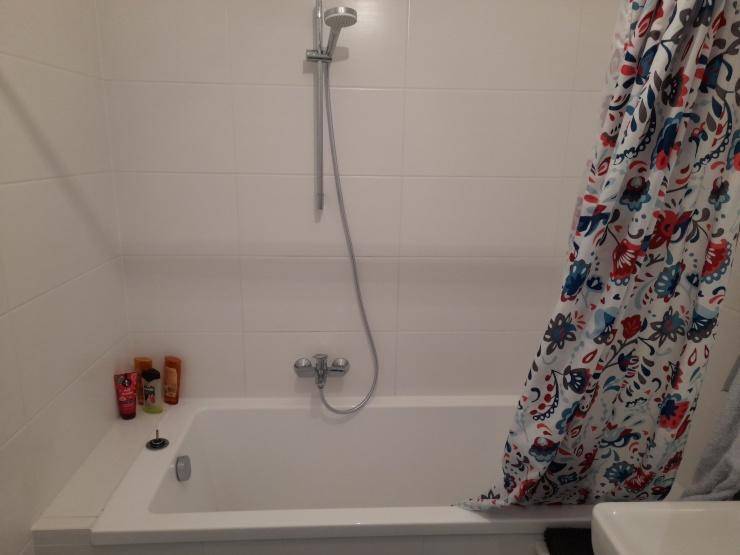 Einfache Badewanne mit Duschvorhang und Handbrause in einem gefliesten Badezimmer.