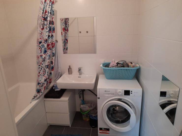 Funktionales Badezimmer mit Badewanne, Waschbecken, Spiegelschrank und Waschmaschine.