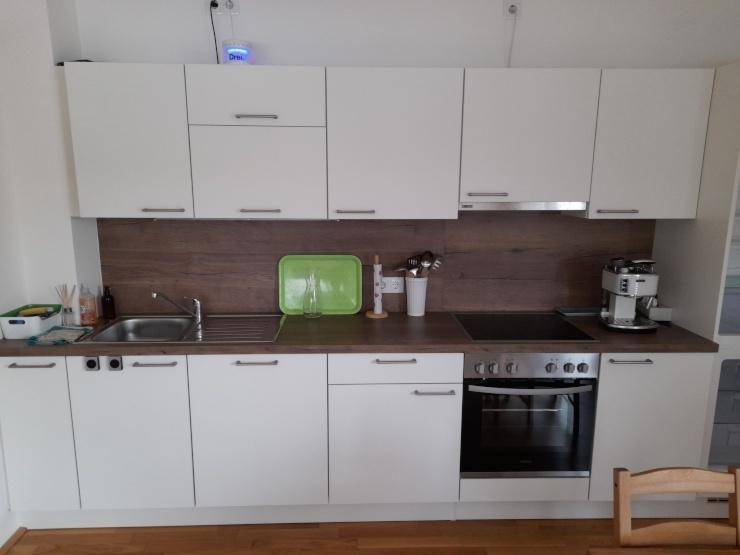 Moderne Einbauküche mit weißen Schränken, Holzoptik-Arbeitsplatte und integrierten Geräten.