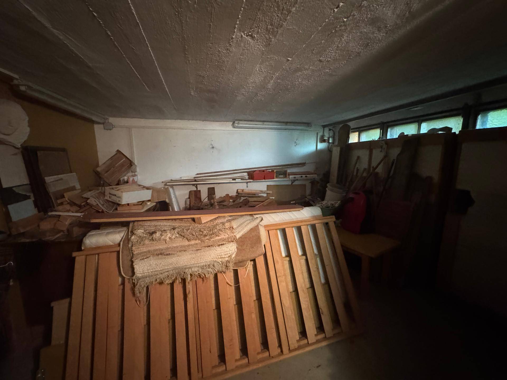 Dunkler Kellerraum mit gestapeltem Holz und verschiedenen Gegenständen, als Lagerfläche genutzt.