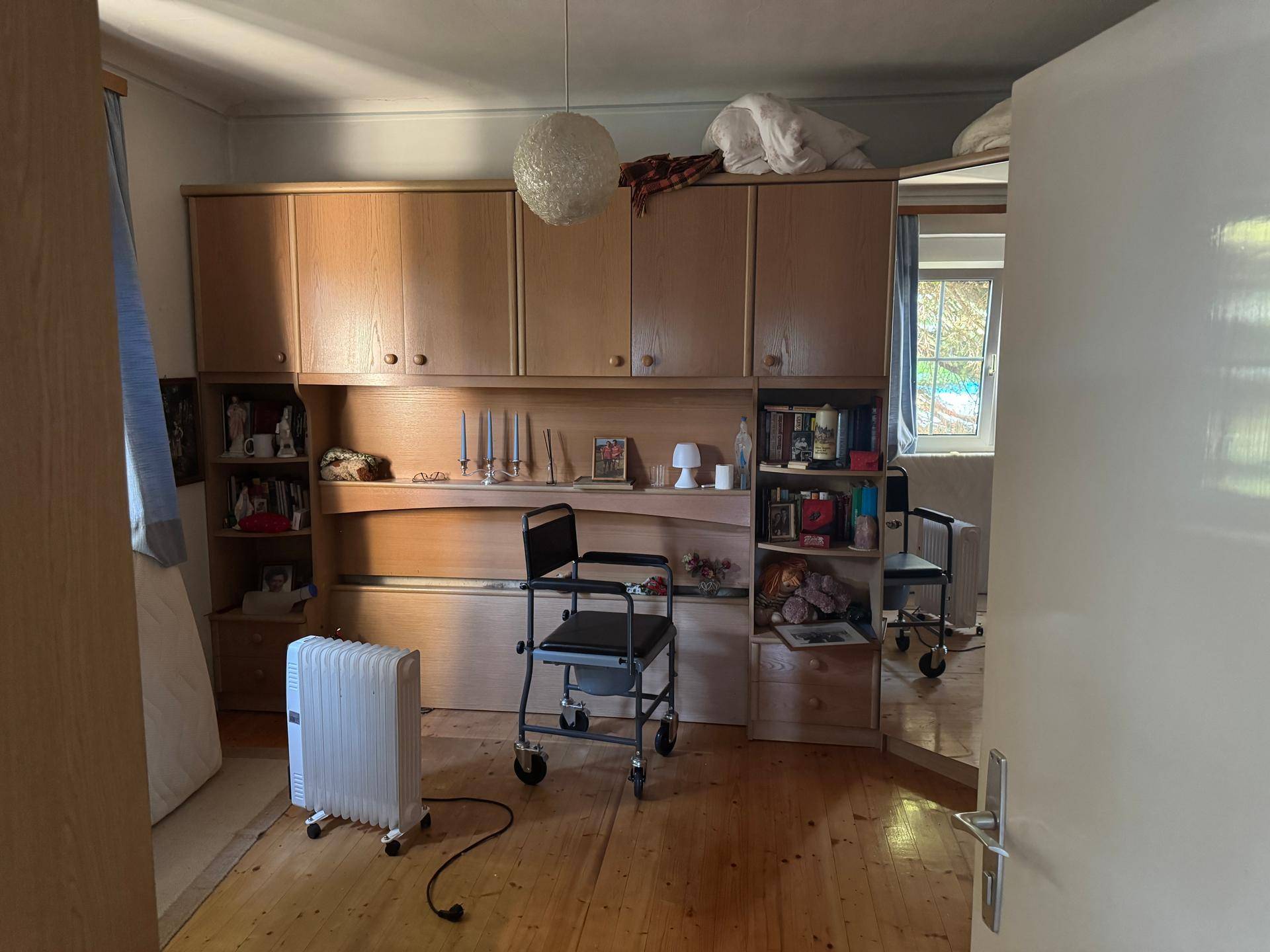 Schlafzimmer mit Einbauschränken, Holzfußboden und einem Fenster mit Blick nach draußen, hell.