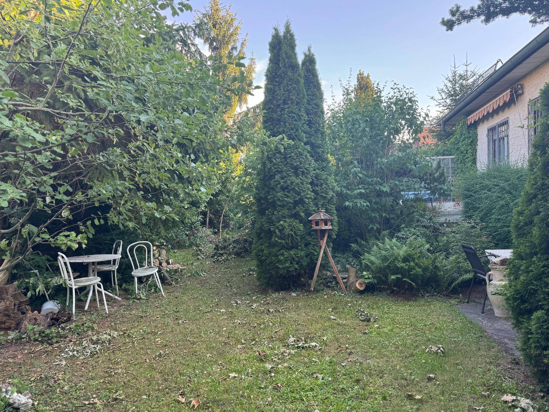Gemütlicher Gartenbereich mit Rasen, Sitzgelegenheiten und einem Vogelhäuschen unter Bäumen.