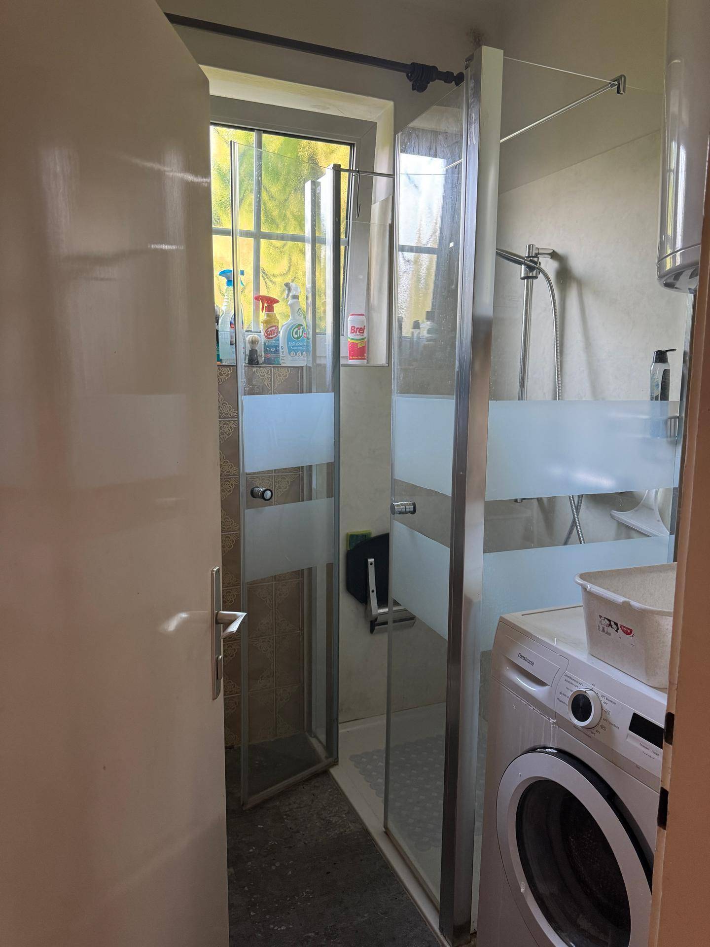 Badezimmer mit Duschkabine und Waschmaschine, durch eine Tür sichtbar, in einfachem Zustand.