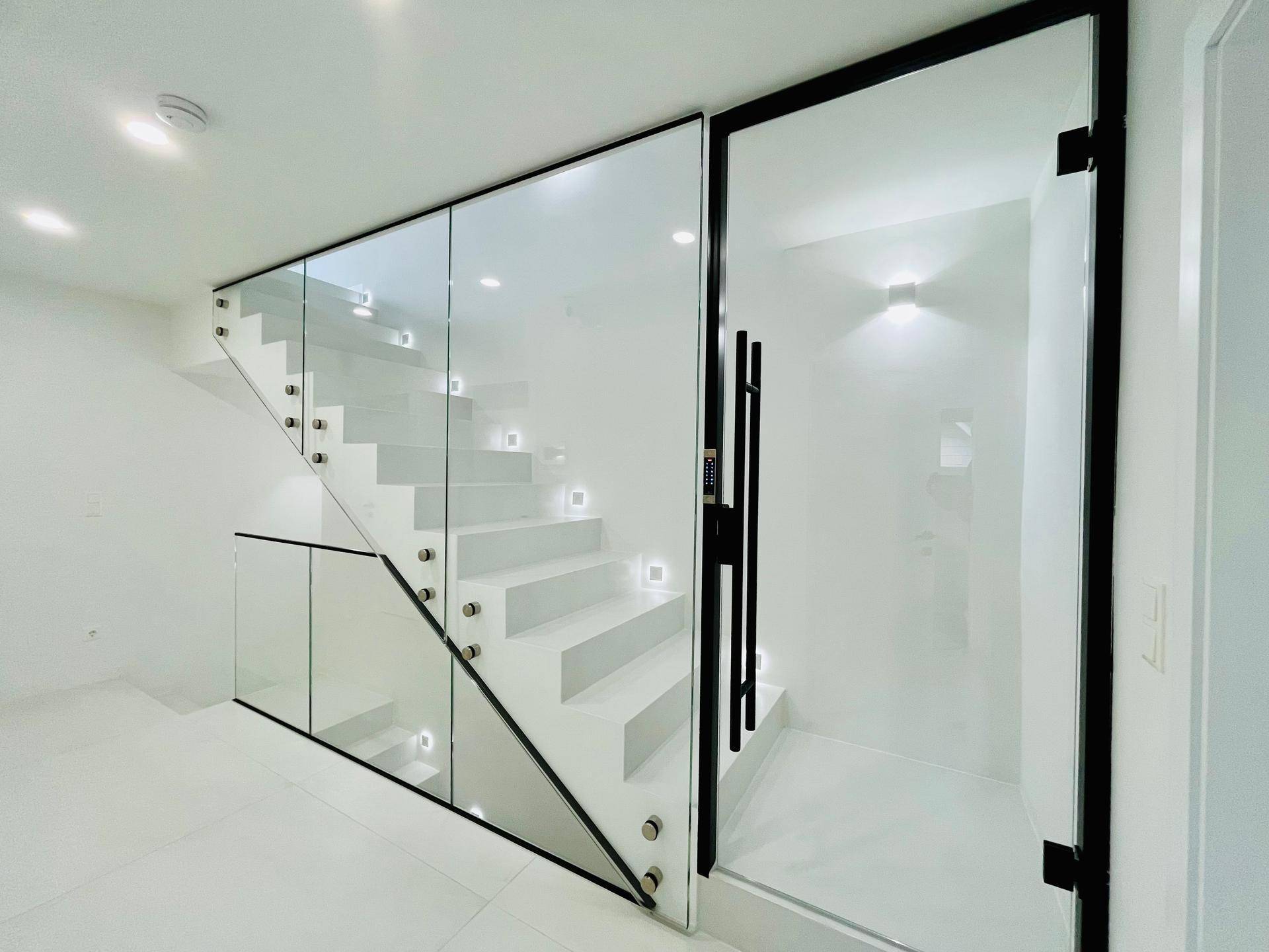 Elegantes Treppenhaus mit Glasgeländer und integrierter Beleuchtung, daneben ein moderner Aufzug.