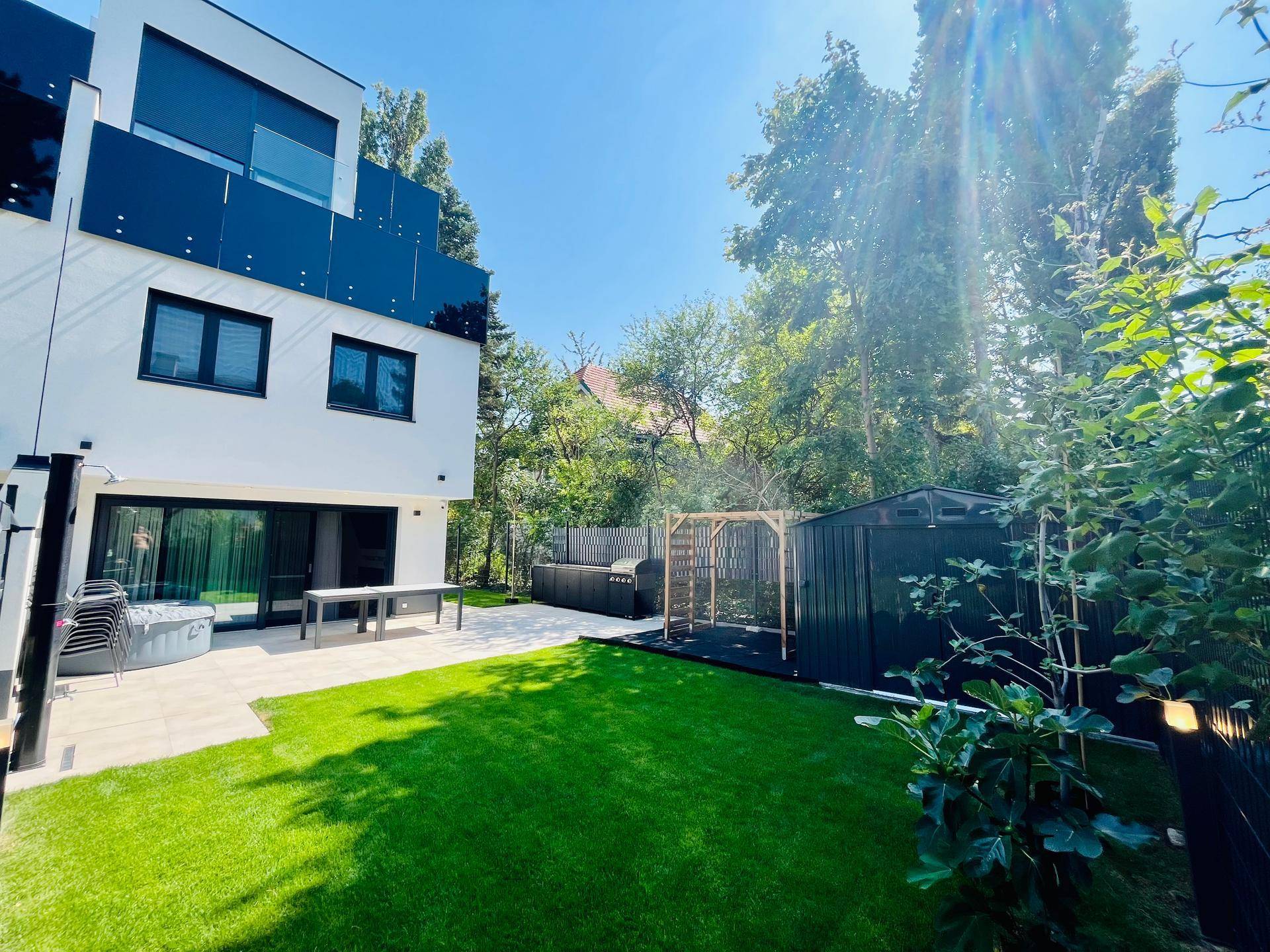 Moderner Gartenbereich mit Rasenfläche, Terrasse, Whirlpool und einem stilvollen Geräteschuppen.