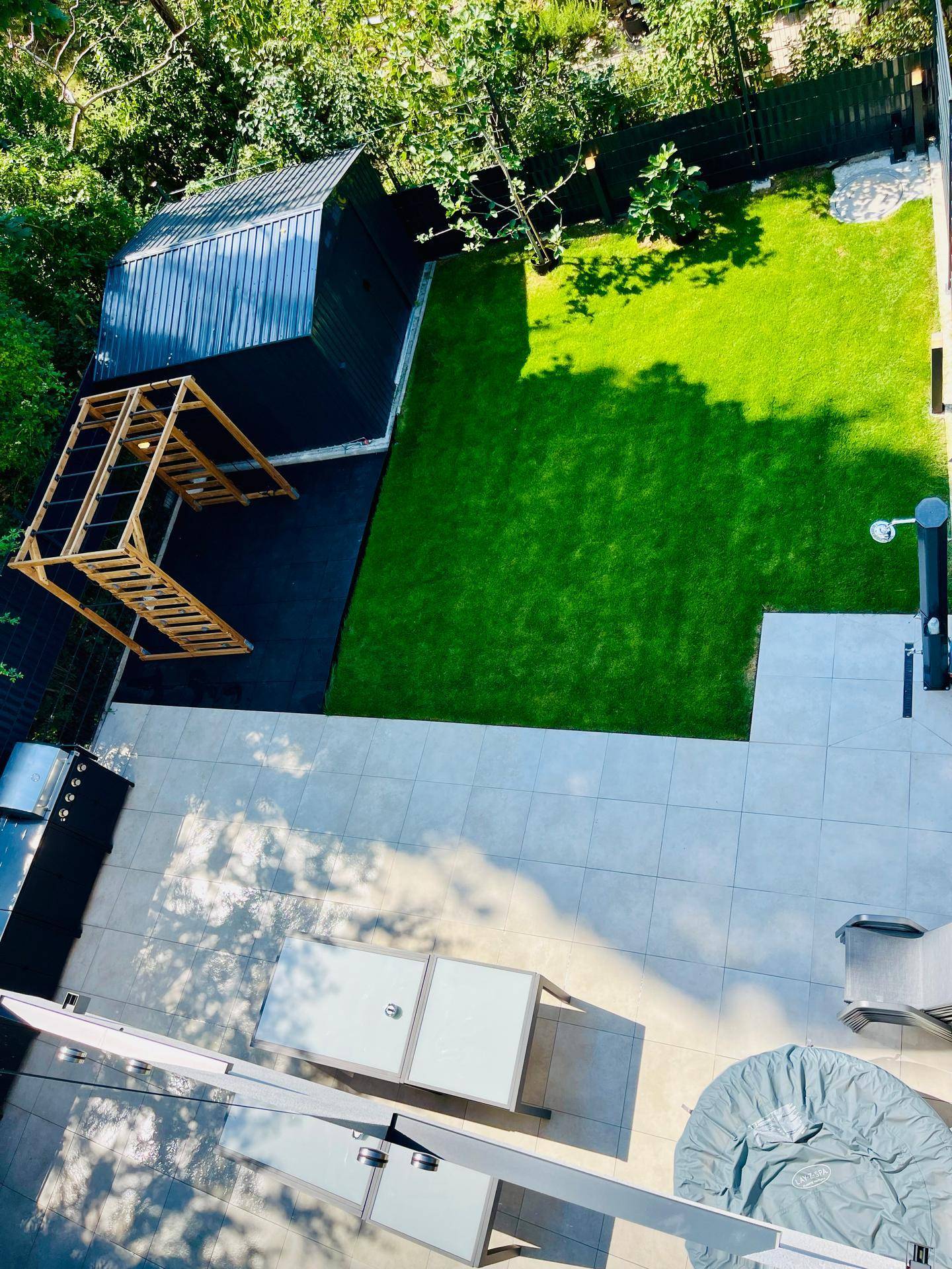 Vogelperspektive des Gartens mit Rasenfläche, großer Terrasse, Whirlpool und Geräteschuppen.