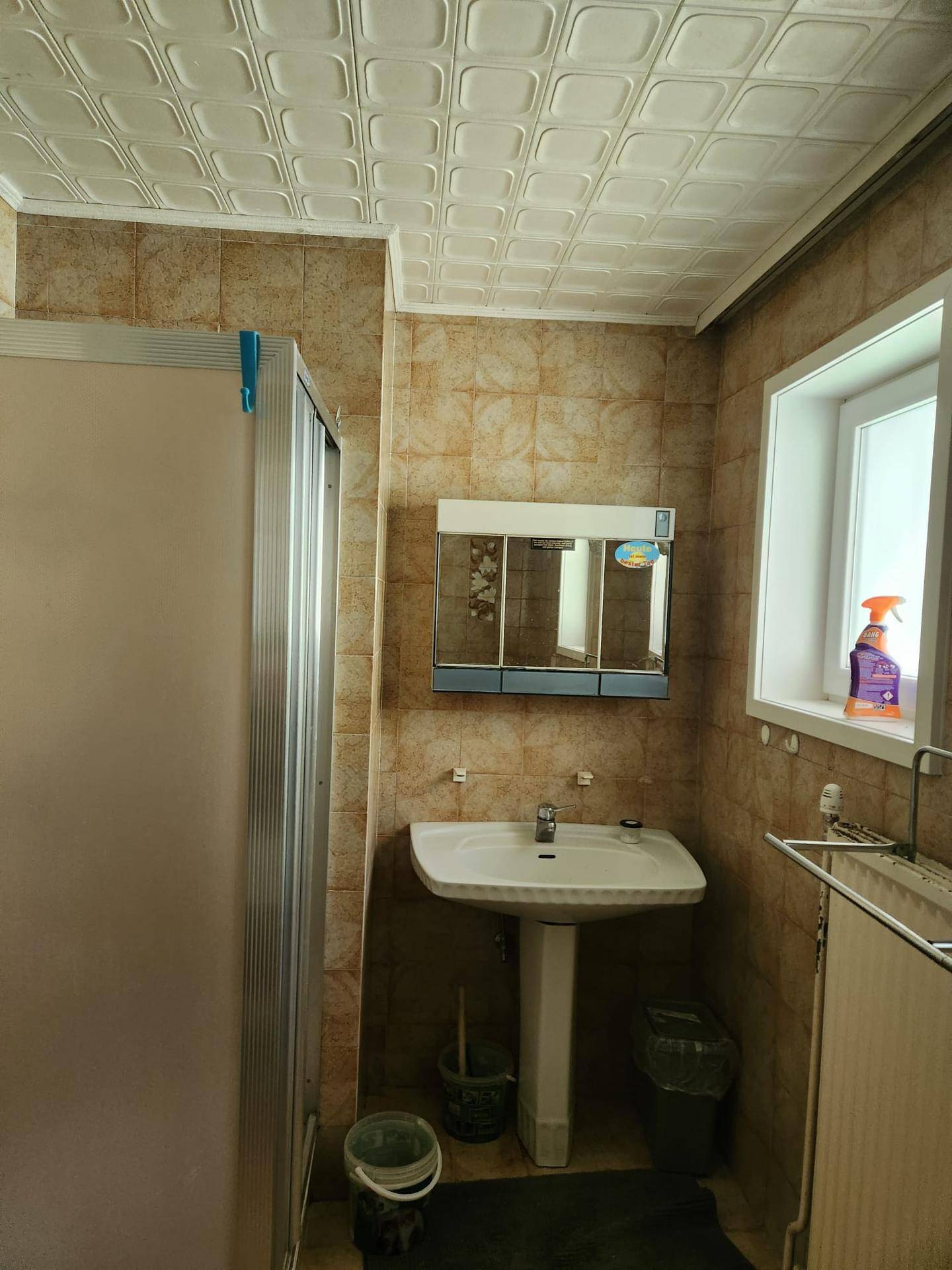 Badezimmer mit beigen Fliesen, Duschkabine, Waschbecken und Fenster.