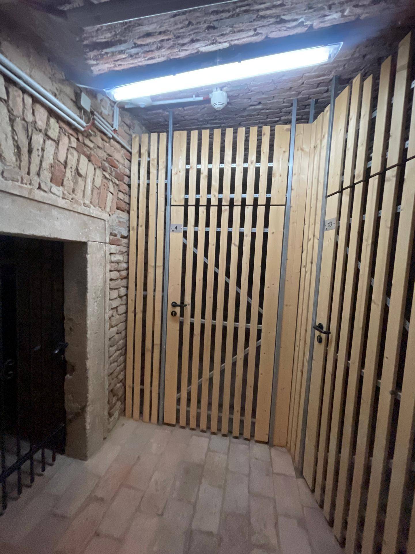 Historischer Kellerraum mit modernen Holzlattenverschlägen und Ziegelwänden.
