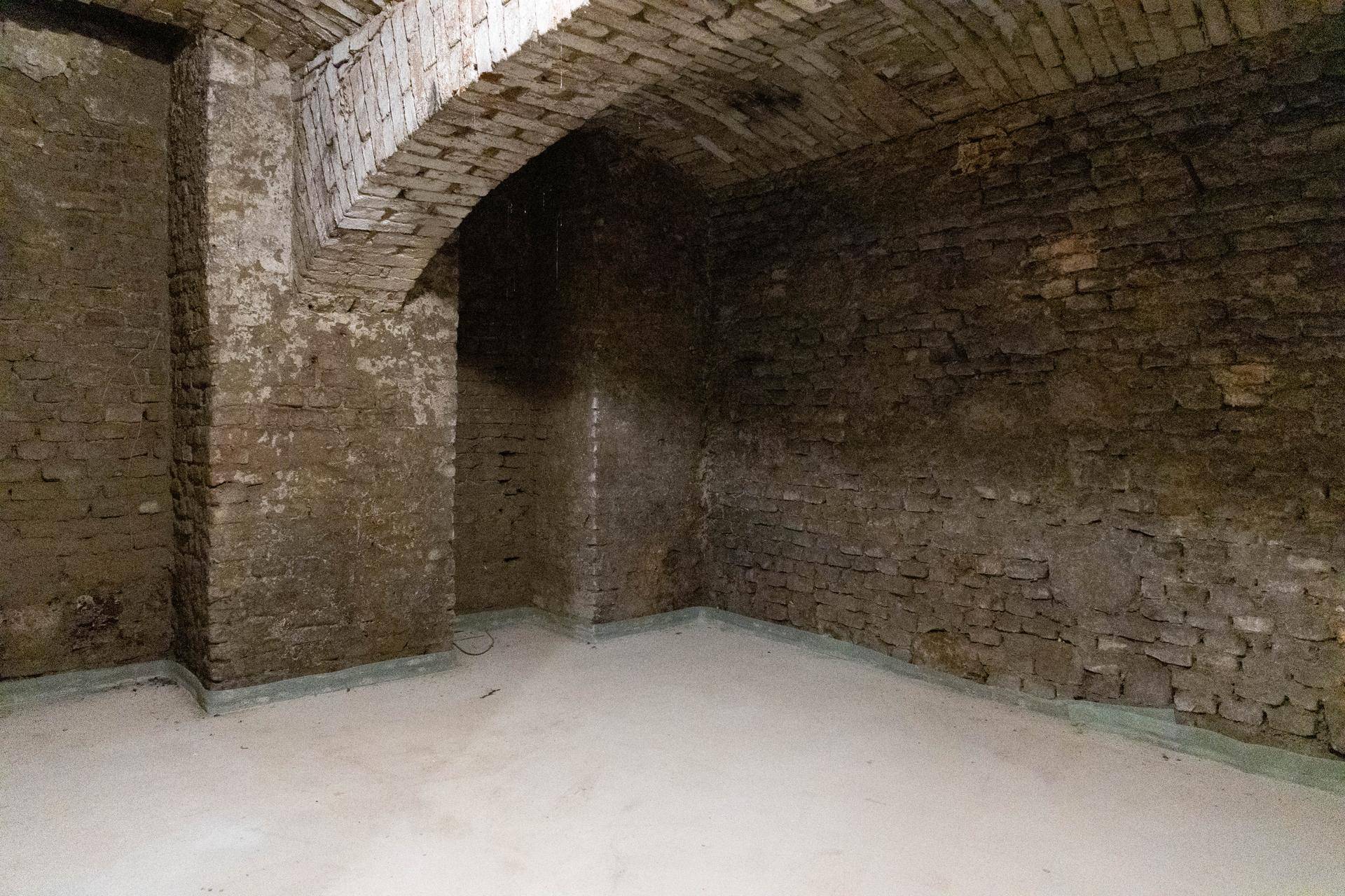 Tiefer Kellerraum mit unverputzten Ziegelwänden und einem markanten Gewölbe, ausgestattet mit einem neuen Betonboden.