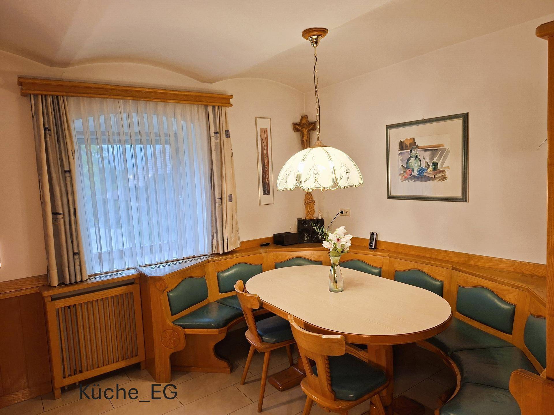 Gemütlicher Essbereich in der Küche mit Eckbank, Holztisch und Fenster mit Vorhängen für natürliches Licht.