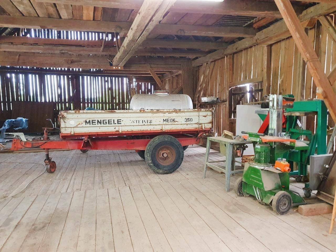 Geräumiger Innenraum der Scheune mit Holzbalken, einem Anhänger und landwirtschaftlichen Geräten.