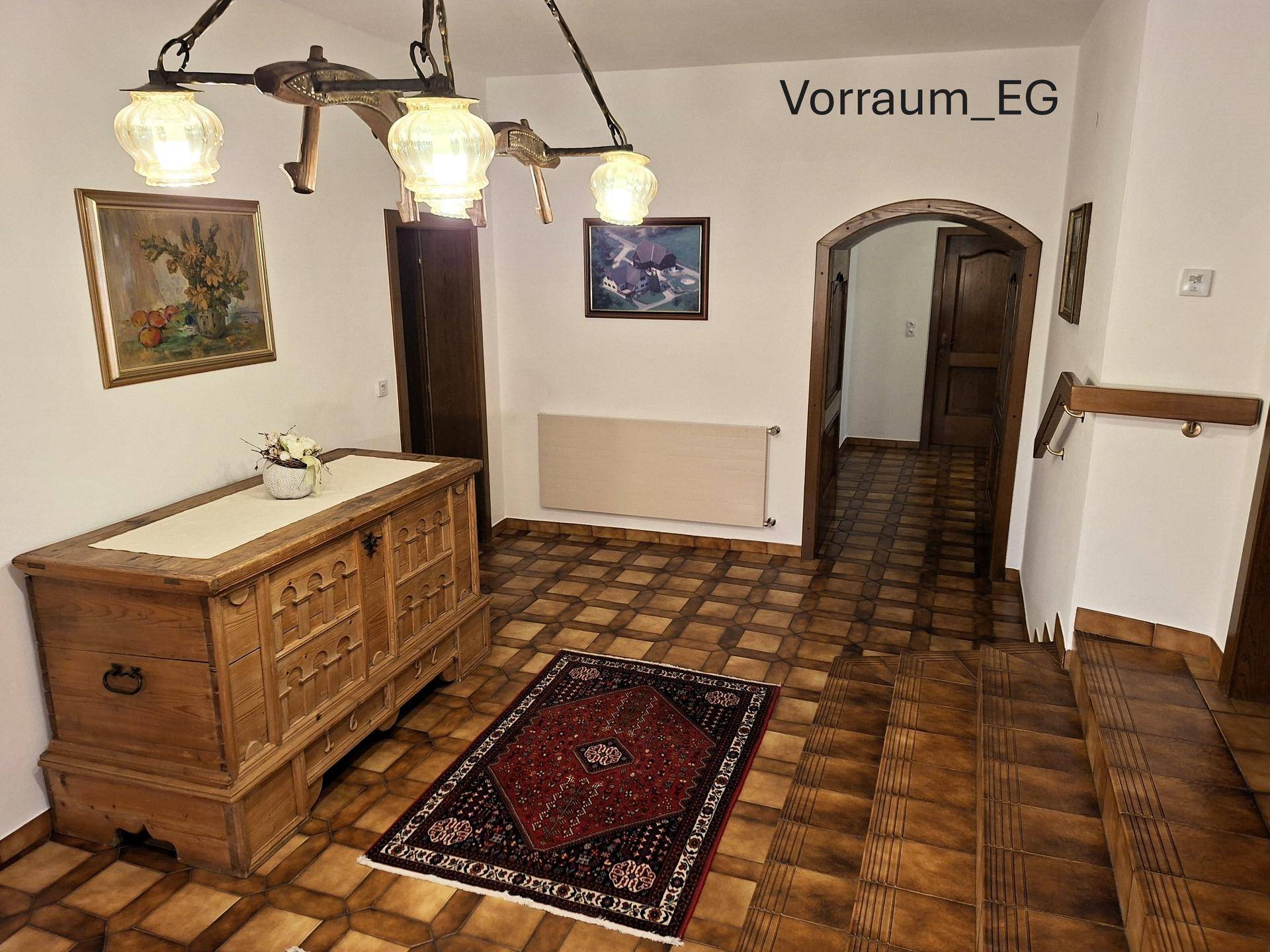 Gemütlicher Vorraum im Erdgeschoss mit Fliesenboden, einer antiken Holzkommode und einem Rundbogen.