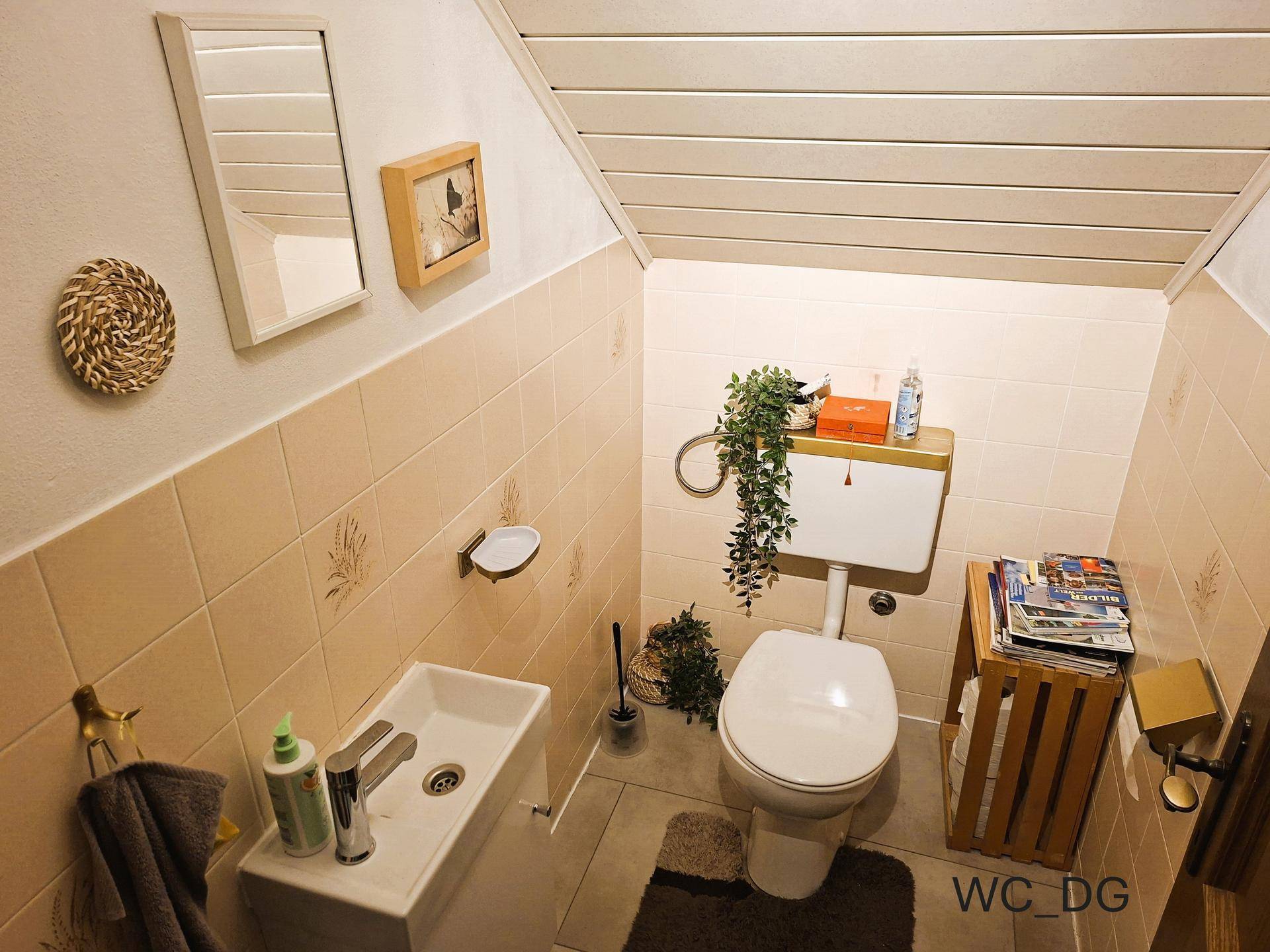 Kleines Gäste-WC im Dachgeschoss mit Toilette, Waschbecken und beigefarbenen Fliesen an den Wänden.