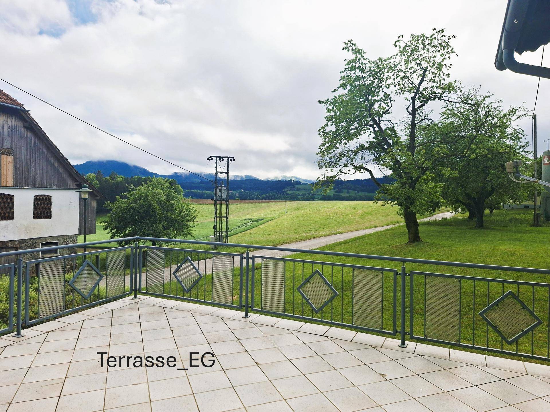 Geräumige Terrasse im Erdgeschoss mit Fliesenboden und weitem Blick auf Felder und Berge.