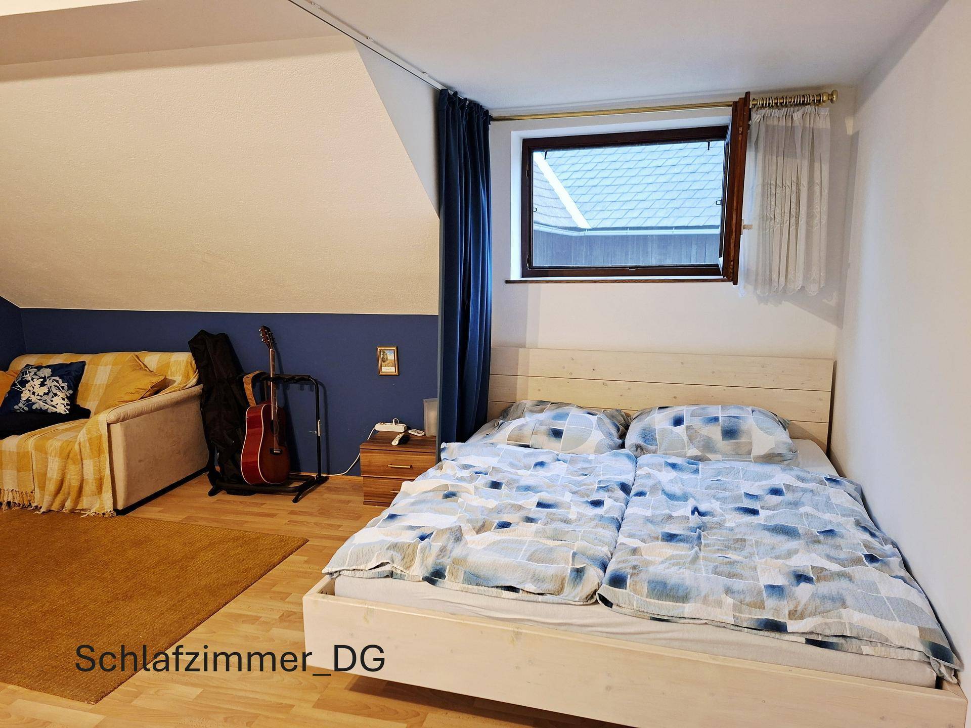 Schlafzimmer im Dachgeschoss mit Doppelbett, Sofa und schrägen Wänden, bietet eine gemütliche Atmosphäre.