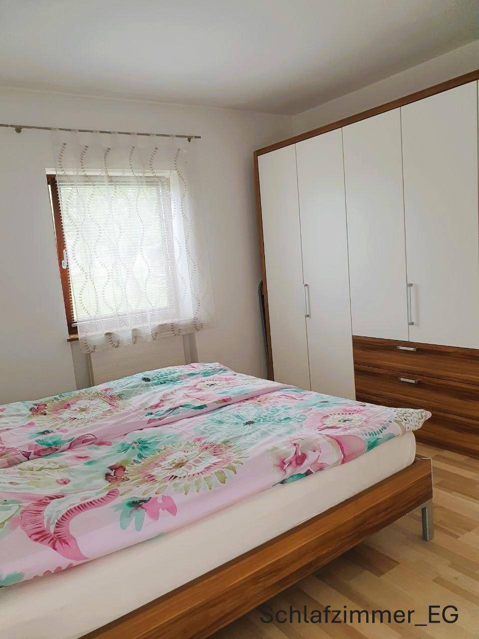 Schlafzimmer im Erdgeschoss mit Bett, floraler Bettwäsche und großem Kleiderschrank mit Holzdetails.