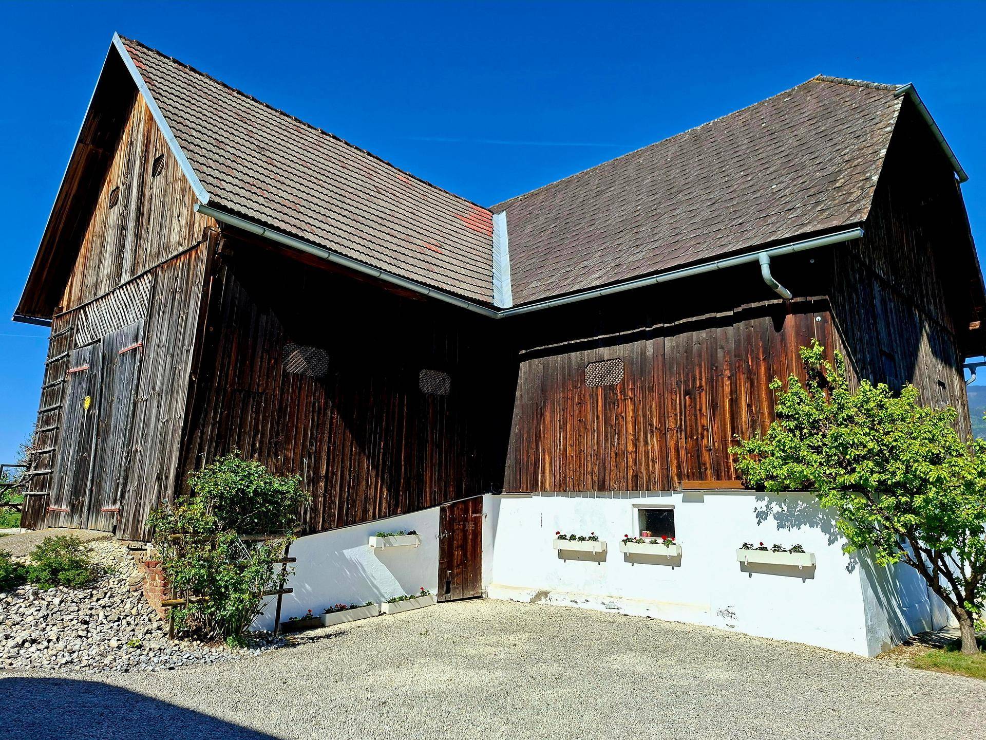 Rustikale Holzscheune mit traditioneller Bauweise und Blumenkästen unter klarem, blauem Himmel.