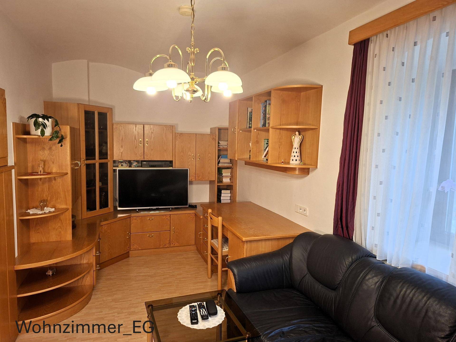 Wohnzimmer im Erdgeschoss mit Holzmöbeln, Fernseher und einer dunklen Couch, klassisch eingerichtet.