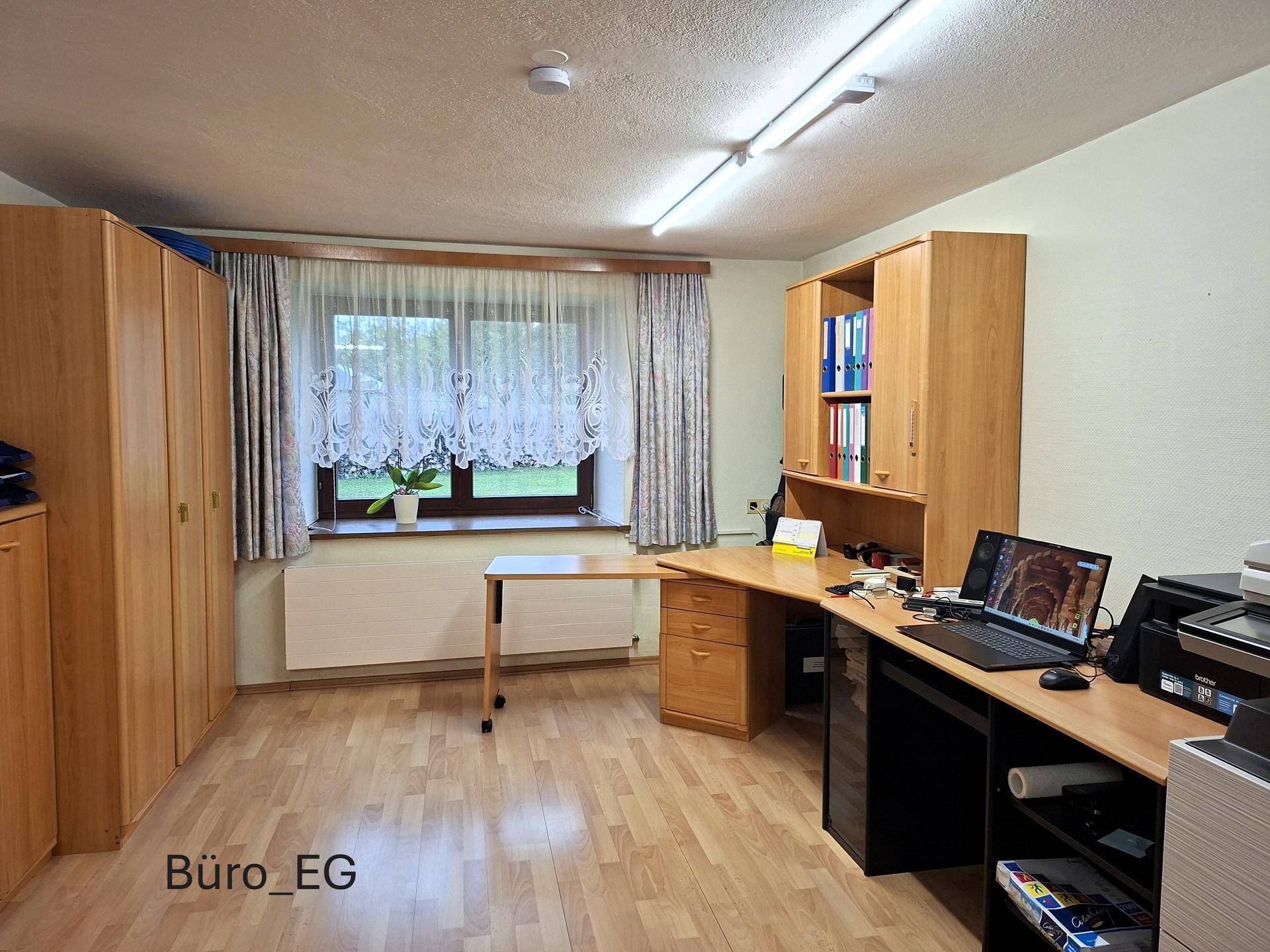 Funktionales Büro im Erdgeschoss mit Holzschreibtischen, Schränken und einem Fenster für Tageslicht.