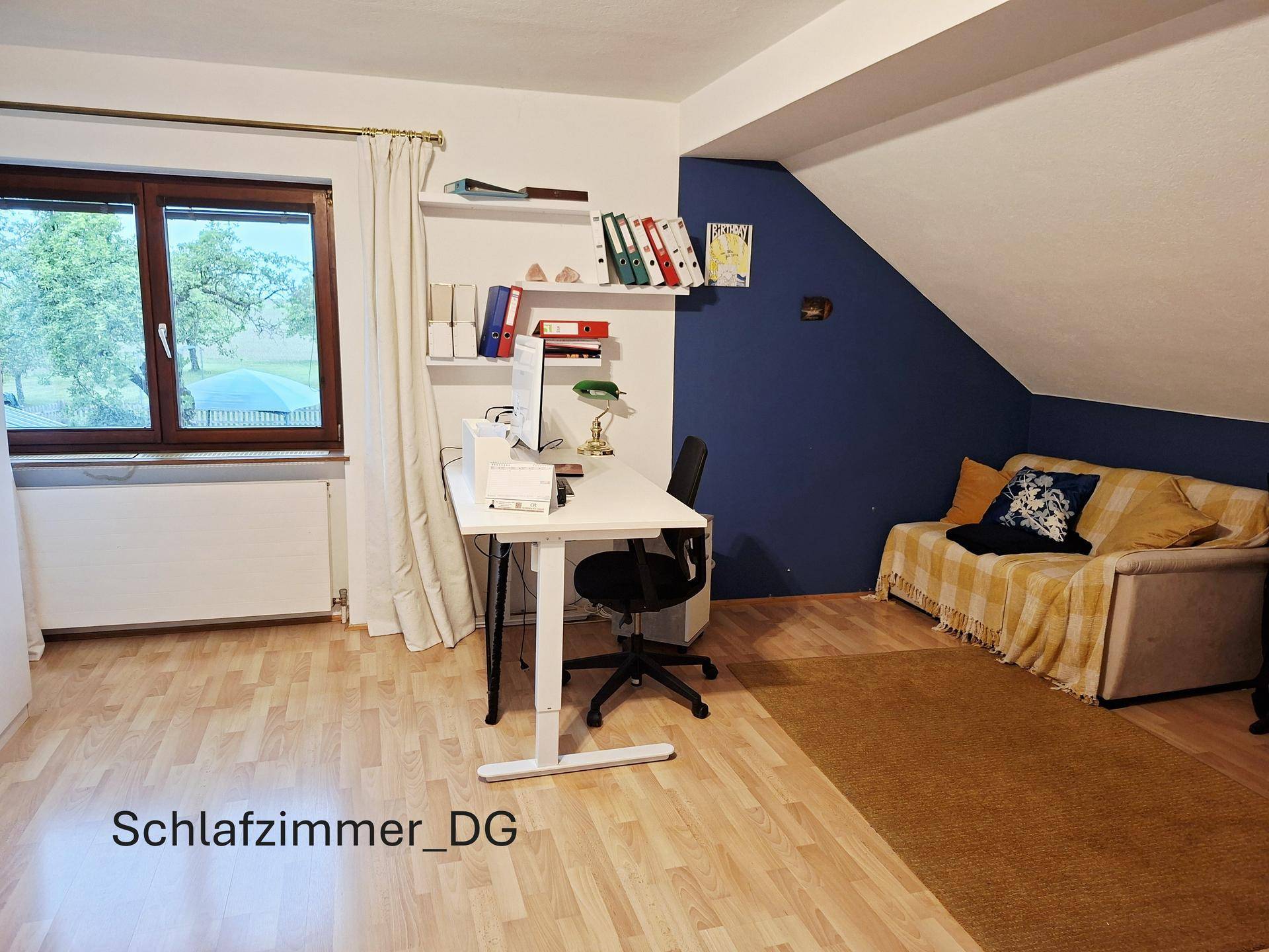 Arbeitsbereich im Dachgeschoss mit Schreibtisch, Sofa und Fenster, ideal für Home-Office oder Studium.